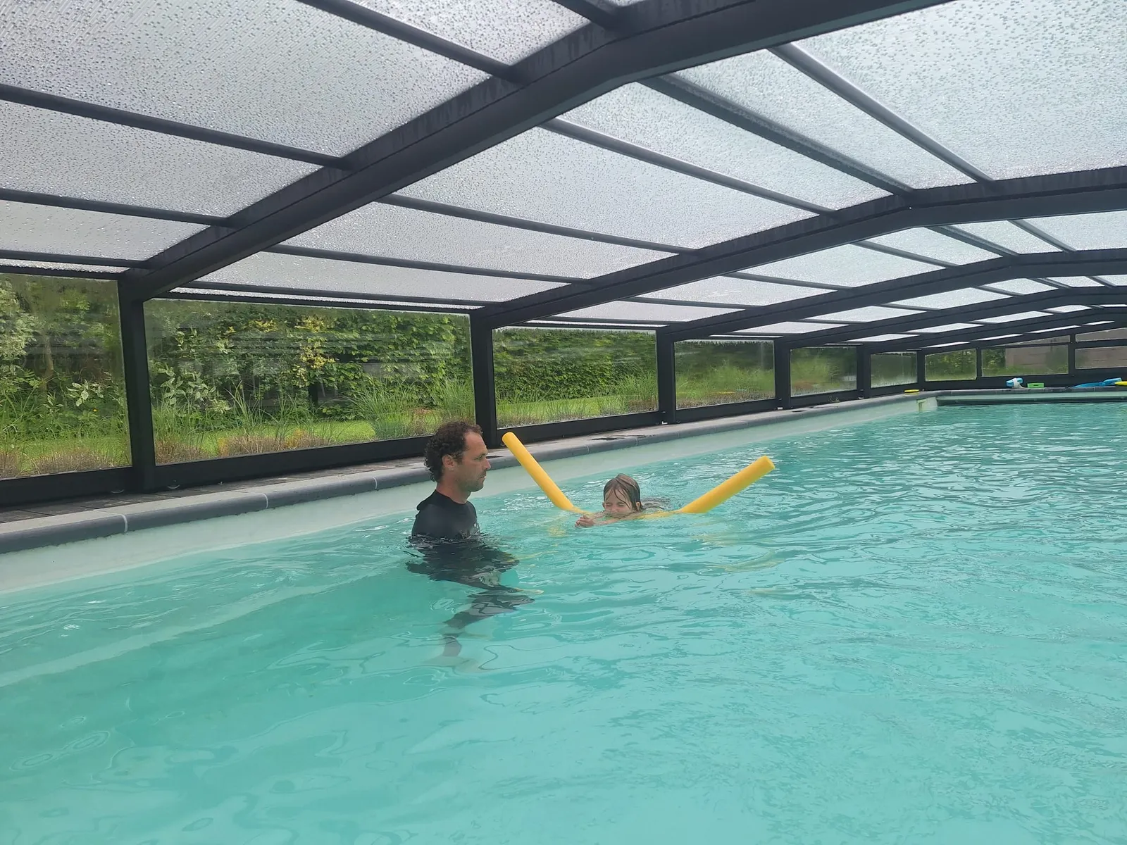Het privézwembad met de overkapping dicht, Klaas in het water met een kind aan een zwemslang